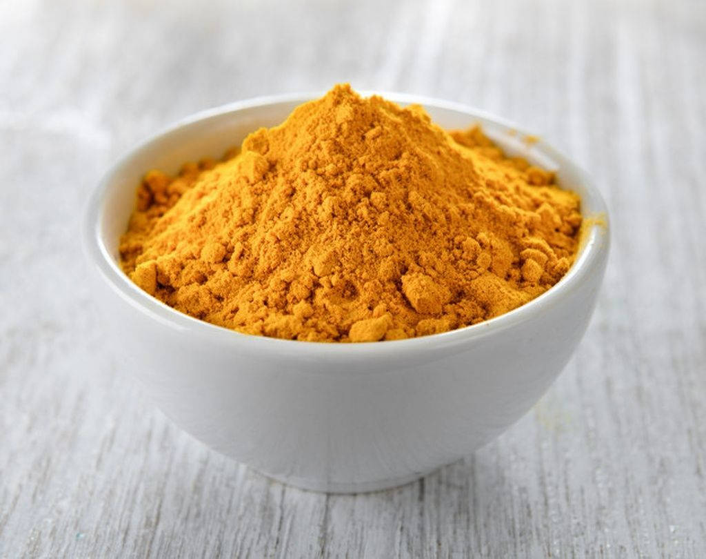 Vibrant Turmeric Powder In A Simple White Bowl Wallpaper