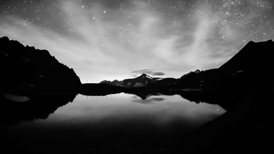 A Black And White Photo Of A Mountain Lake With Stars Wallpaper