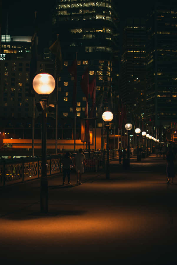 A City At Night With People Walking Along The Sidewalk Wallpaper