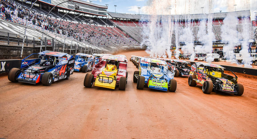 A Group Of Dirt Track Cars Driving In A Stadium Wallpaper