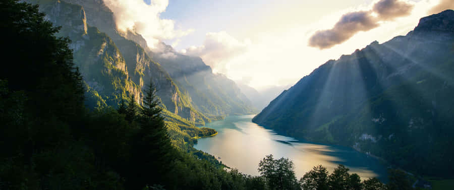 A Lake With Sun Rays Shining Through The Clouds Wallpaper