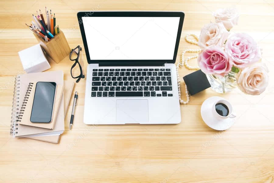 A Laptop, Phone, Flowers And Other Office Supplies On A Wooden Desk Wallpaper