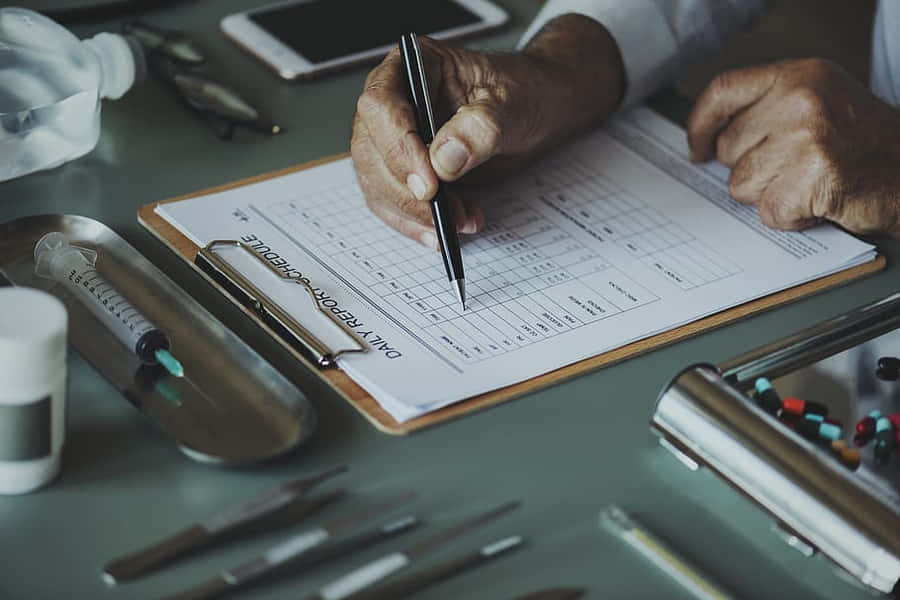 A Man Writing On A Clipboard With Medical Supplies Wallpaper
