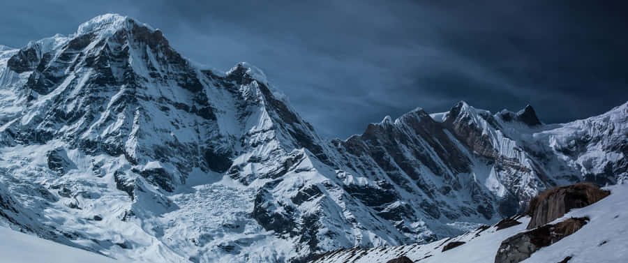 A Mountain Covered In Snow With A Cloudy Sky Wallpaper