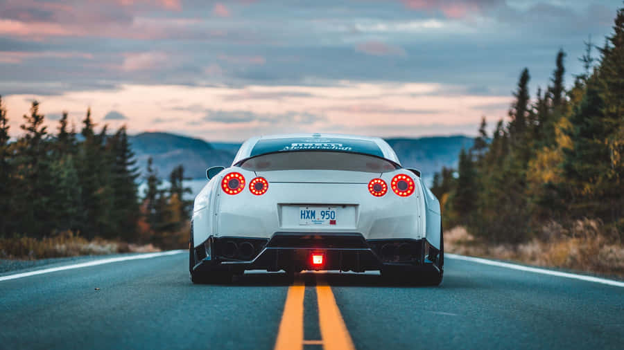 A White Sports Car Driving Down A Road Wallpaper