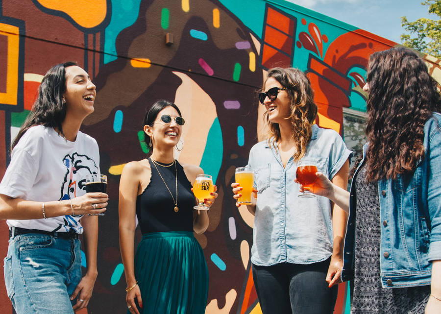 Four Women Holding Drinks While Laughing Together During Daytime Wallpaper