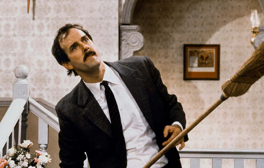 John Cleese With Broom Comedic Scene Wallpaper