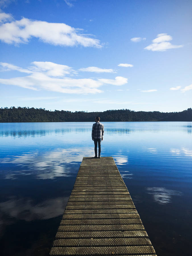 Man Standing On Lake Dock Watching Water Under Blue Sky During Daytime Wallpaper