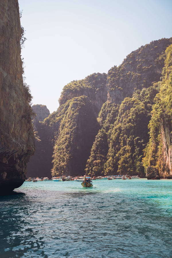 People Riding Boat On Sea Near Brown Rocky Mountain During Daytime Wallpaper