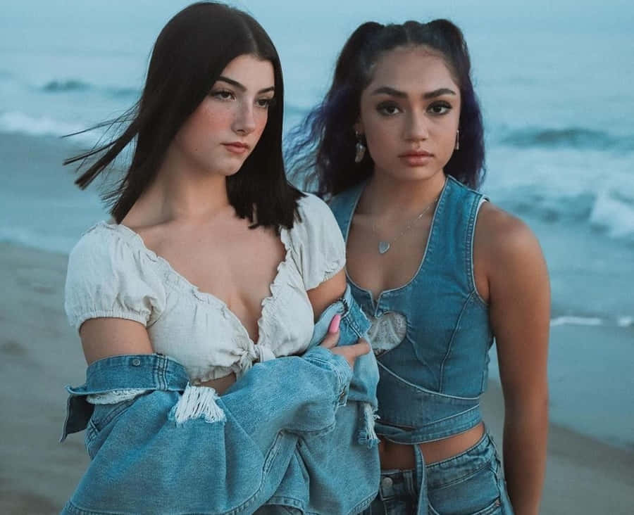 Two Women Standing On The Beach Wearing Denim Wallpaper