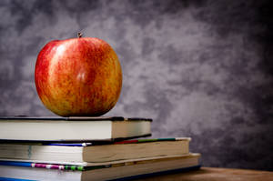 A Colorful Collection Of Books With A Single Apple Popping Against The Background. Wallpaper