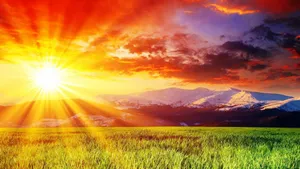 A Colorful Sun Rising Over A Green Field Wallpaper