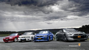 A Display Of Illustrious Jdm Performance Cars Against A Cloudy Sky Wallpaper