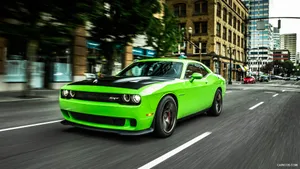 A Green Dodge Challenger Driving Down A City Street Wallpaper