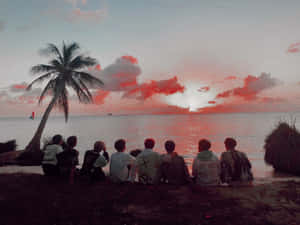 A Group Of People Sitting On The Beach Watching The Sunset Wallpaper