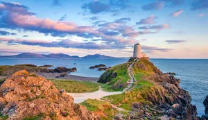A Lighthouse Sits On Top Of A Rocky Cliff Wallpaper