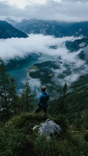 A Man Standing On A Mountain Overlooking A Lake Wallpaper