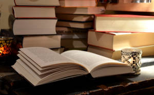 A Picture Of An Open Book On A Desk, Surrounded By Other Reference Books Wallpaper