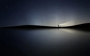 A Picturesque View Of A Lighthouse Glowing Brightly In The Night Sky. Wallpaper