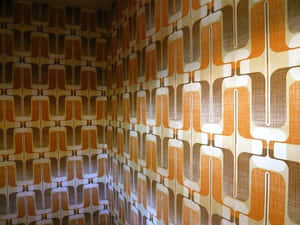 A Room With A Wall Covered In Orange And Brown Wallpaper Wallpaper