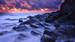 A Stunning Oranges And Pinks Sunset Over Rugged Cliffs Wallpaper