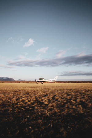 A Tinny White Plane Waiting For Takeoff In Open Field Wallpaper