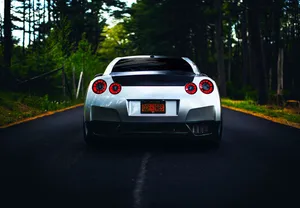 A White Sports Car Driving Down A Road In The Woods Wallpaper