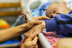 A Woman Is Helping An Elderly Person In A Hospital Bed Wallpaper