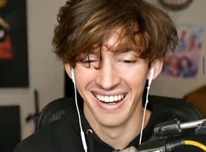 A Young Man Is Smiling While Wearing Headphones Wallpaper