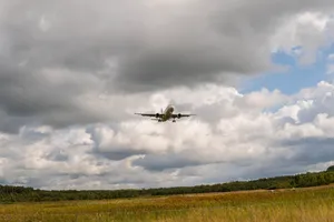 Airplane Flying Over Green Grass Field Under White Clouds During Daytime Wallpaper