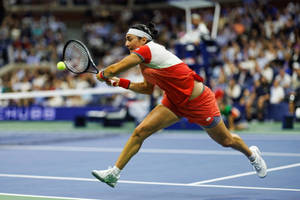 Caption: Ons Jabeur Leaping With Determination In A Competitive Tennis Match. Wallpaper