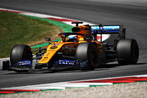 Carlos Sainz Jr. Speeding On The Track In His Yellow F1 Race Car Wallpaper