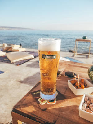 Clear Heineken Glass Filled With Yellow Liquid On Wooden Table Wallpaper