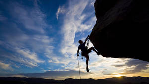 Climber Conquering A Mountain Peak At Sunset Wallpaper