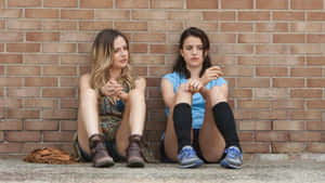 Contemplative Friends Sitting Against Brick Wall Wallpaper