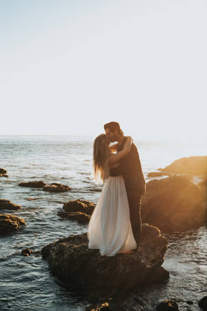 Couple Hugging And Kissing On Rock At Sea Wallpaper