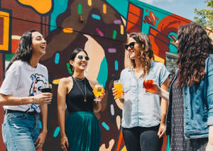 Four Women Holding Drinks While Laughing Together During Daytime Wallpaper