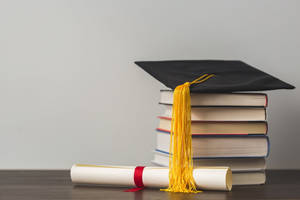 Graduate Cap On Top Of Reference Books Near A Diploma Wallpaper