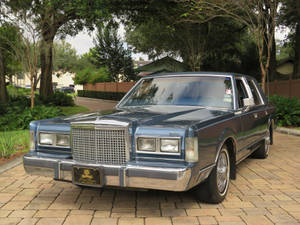 Majestic 1986 Lincoln Town Car Parked On A Paved Driveway Wallpaper