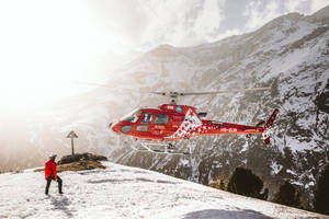 Majestic Helicopter Landing On A Snowy Mountain Peak Wallpaper