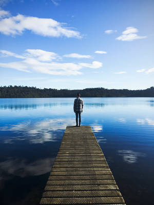 Man Standing On Lake Dock Watching Water Under Blue Sky During Daytime Wallpaper