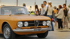 Men And Women Standing Beside A Yellow Car Wallpaper