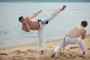 Muscular Men Having A Beach Capoeira Match Wallpaper