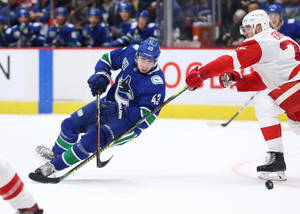 Quinn Hughes Dribbling Hockey Puck Against Player From Detroit Red Wings Wallpaper