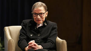 Ruth Bader Ginsburg Seated On Couch Wallpaper
