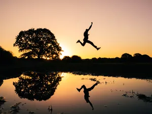 Silhouette Photo Of Man Jumping On Body Of Water During Golden Hour Wallpaper