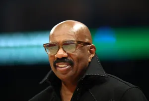 Steve Harvey Smiling In Coat And Sunglasses Wallpaper