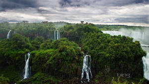 Take In A Peaceful View Of A Green Forest, Surrounded By Majestic Waterfalls Wallpaper