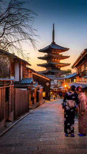 Two Women In Traditional Kimono Walking Down A Street Wallpaper