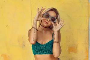 Woman In Blue Bralette Holding Sunglasses Putting On Her Eyes Wallpaper